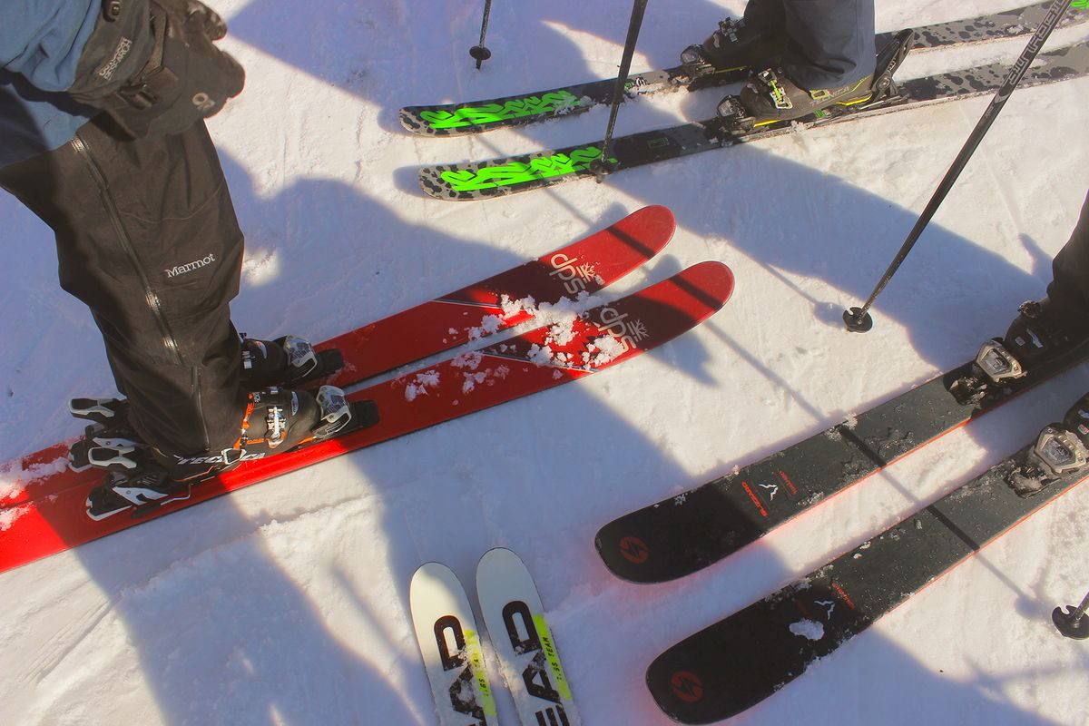 Several pairs of skis with ski boots and poles on the snow.