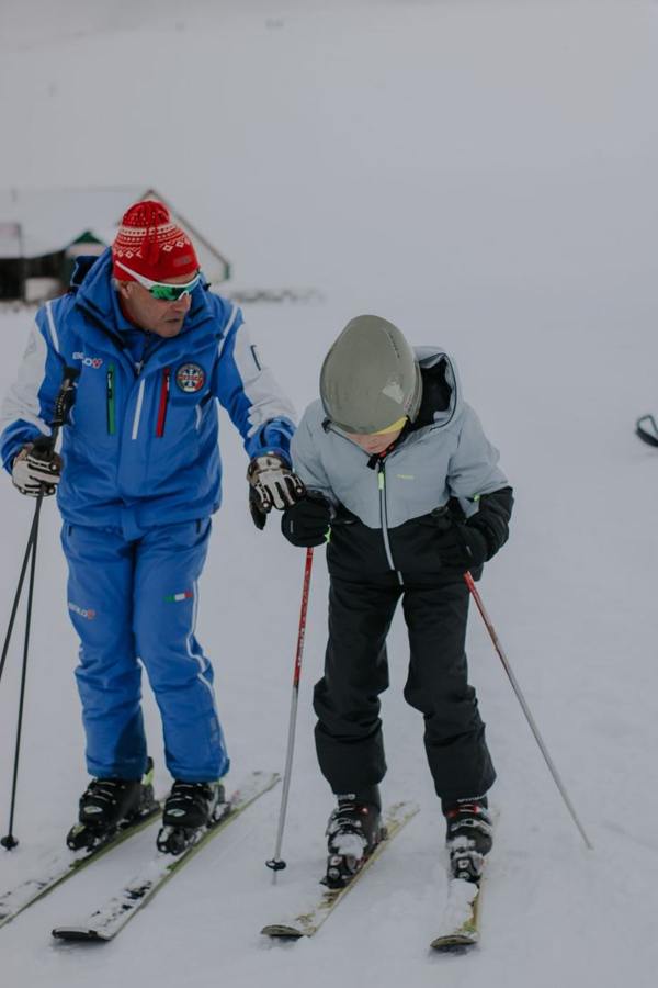 A person accompanying a child on skis in the snow.