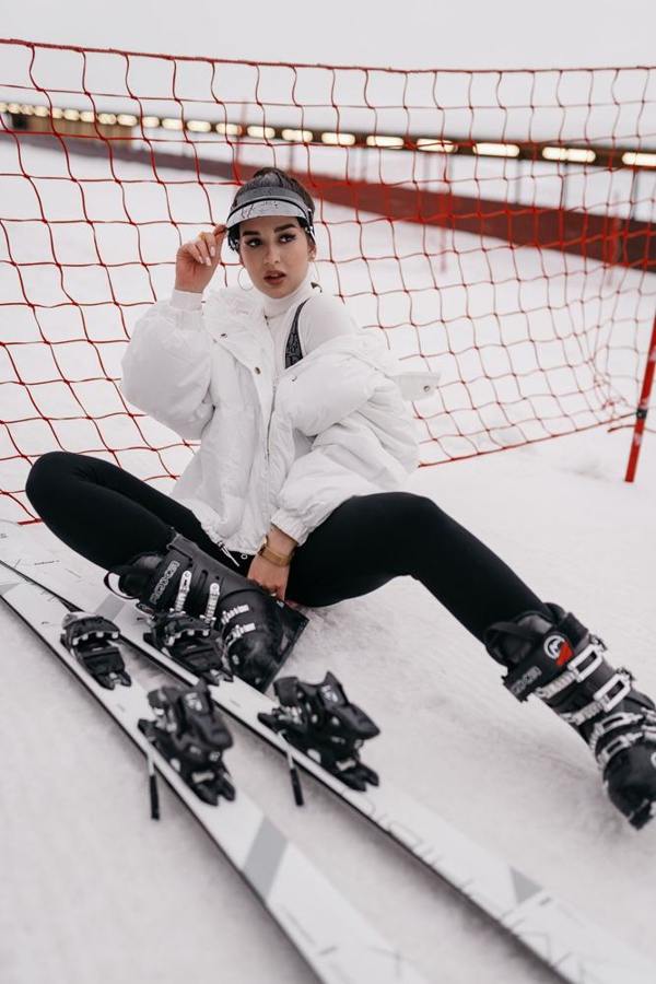 A woman sits in the snow wearing ski boots beside her skis.
