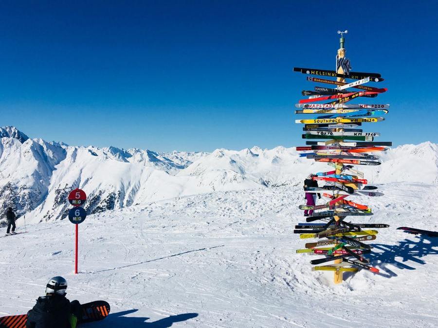 A colourful direction post and piste markers with snowy mountains beyond.
