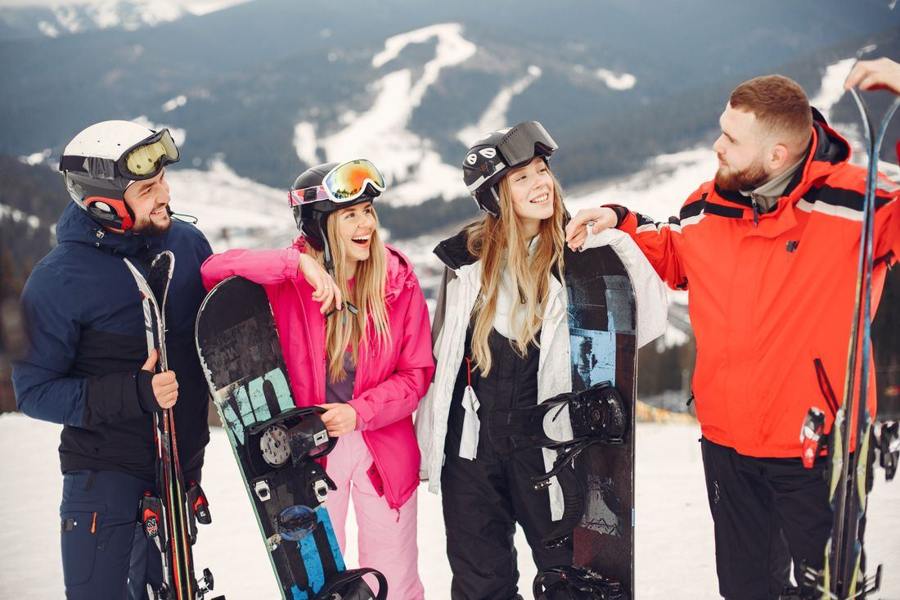 Four people with skis and snowboards standing together on snow.
