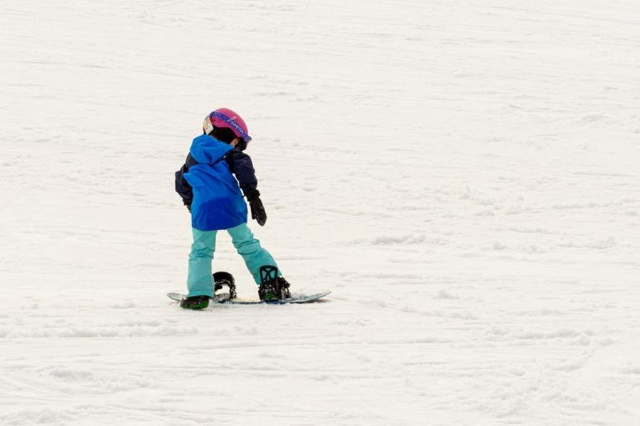 A child stands on a snowboard on a gentle snowy slope.
