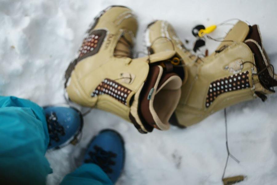 Two pairs of snowboard boots stand on snowy ground.