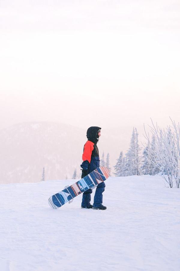 A person carries a snowboard through a snowy landscape.