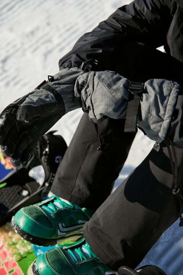 A seated snowboarder pulls on a black snow glove.