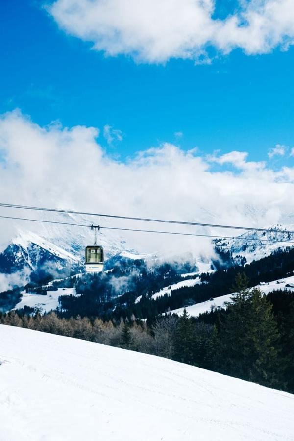 A gondola travels above a snowy slope with mountains beyond.
