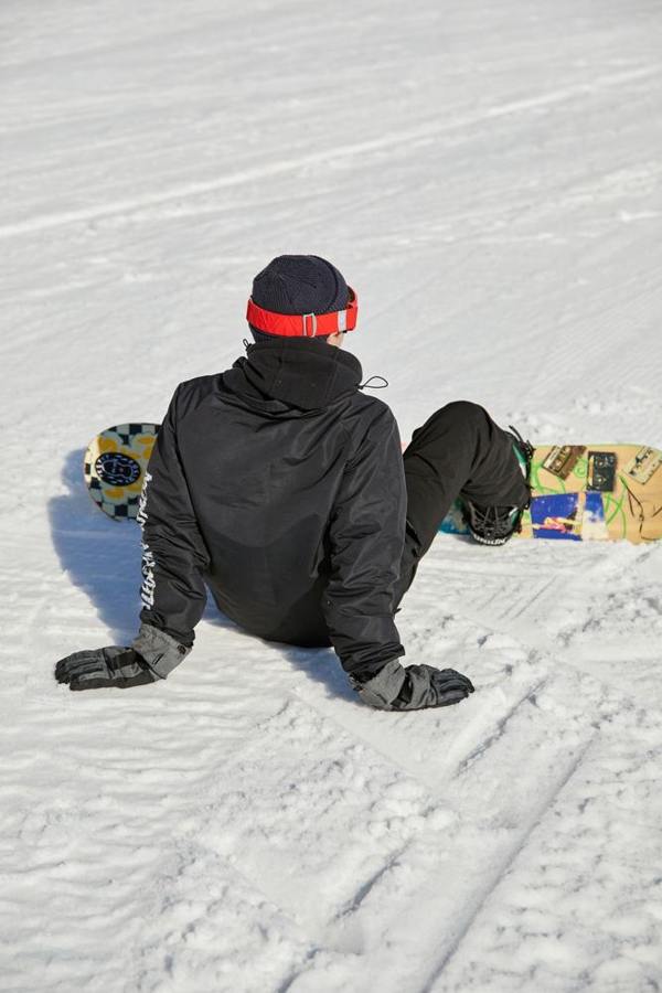 A snowboarder sits on the snow with a board across the slope.