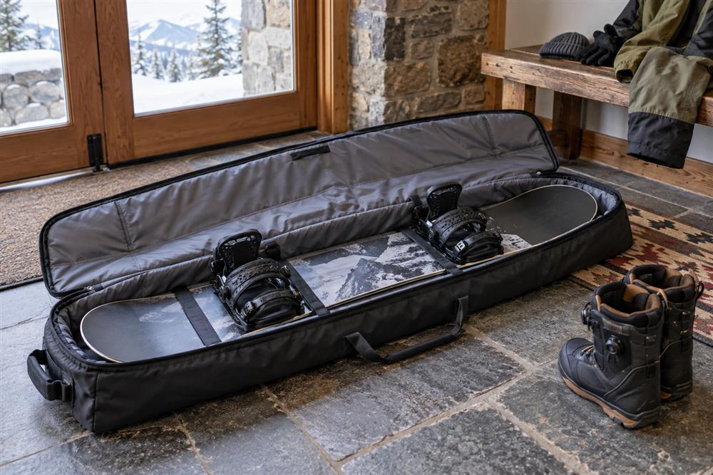 An open padded snowboard travel bag holding a snowboard with boots beside it