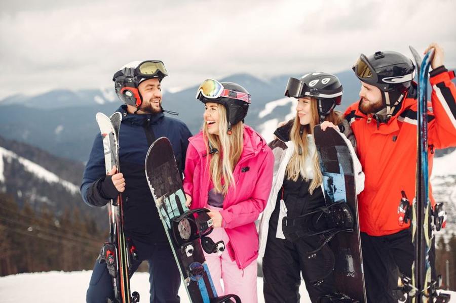 Four winter sports participants stand together with snowboards and skis.