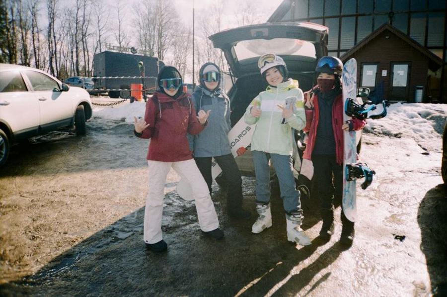 A group stands with snowboards in a snowy parking area.