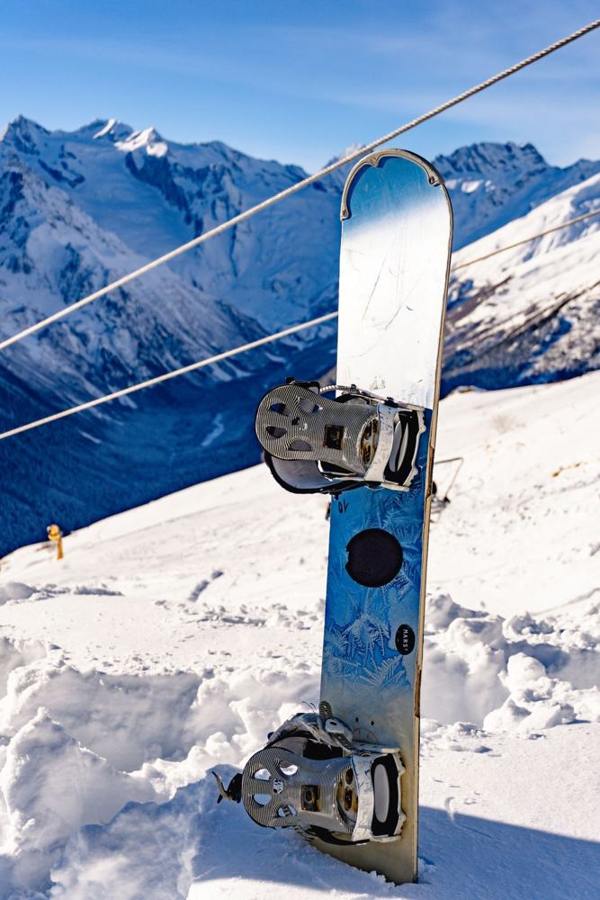 A snowboard with bindings stands upright beside a mountain piste.