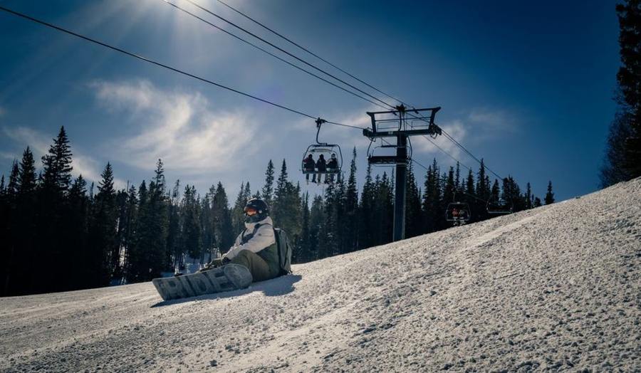 A snowboarder sits on a sunny slope below a chairlift.