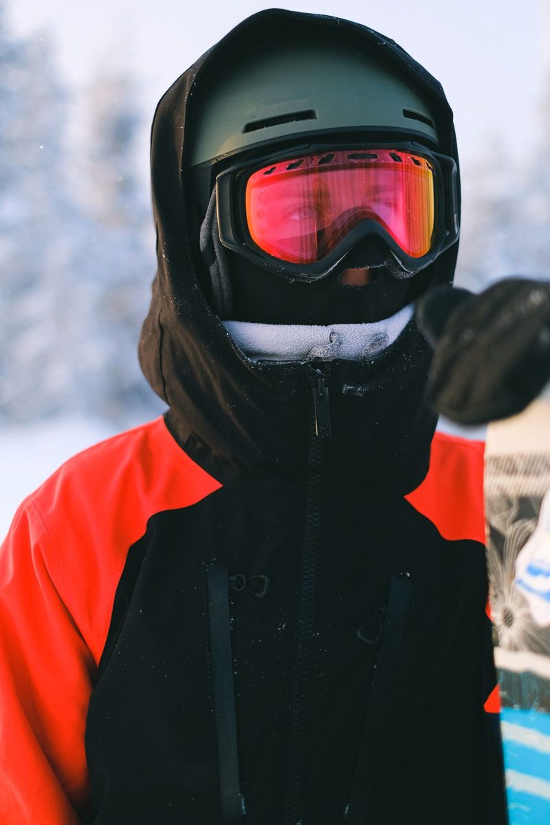 A person wearing a black ski helmet and red-lensed ski goggles.