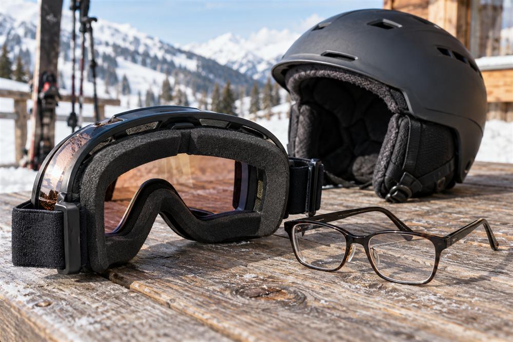 Ski goggles with visible padding, prescription glasses and a helmet on a wooden table