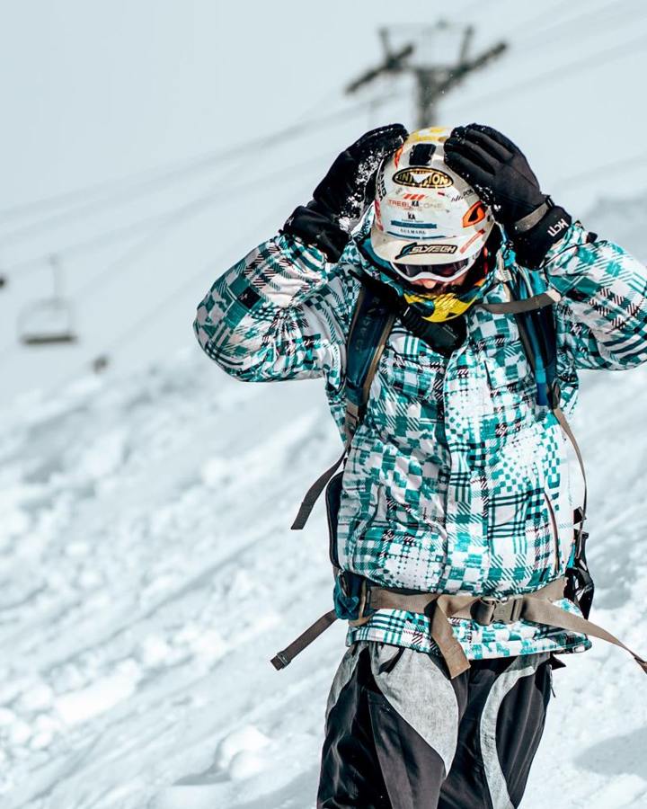 A winter sports participant adjusts a helmet with both hands.
