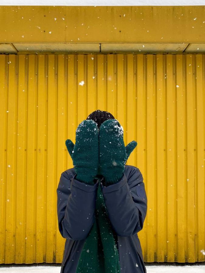 A person holds snow-covered mittens in front of their face.