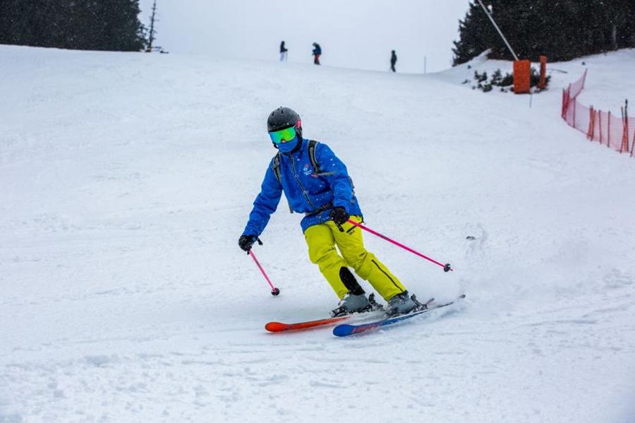 A skier in a blue jacket and yellow ski trousers makes a turn.