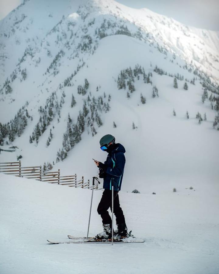 A skier checks a smartphone on a snowy slope.