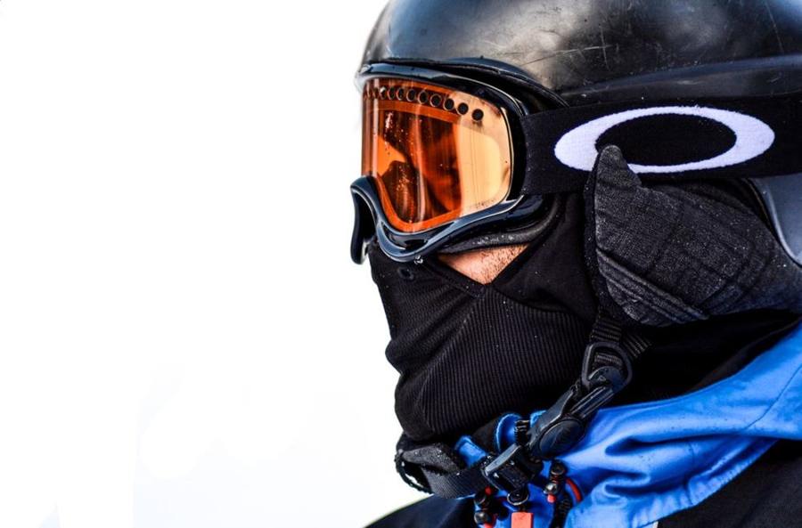 A person wears a black face covering below ski goggles.