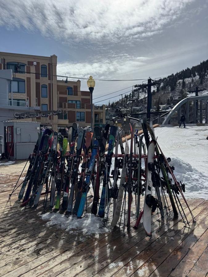 Numerous skis stand in a rack beside a snowy piste.