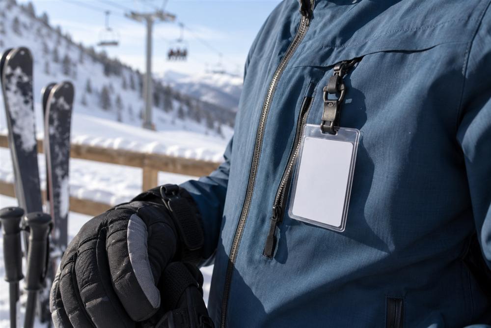 A compact ski lift pass holder with a short clip attached to a ski jacket