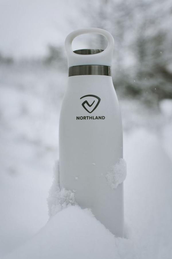 A white drink bottle stands on snowy ground.