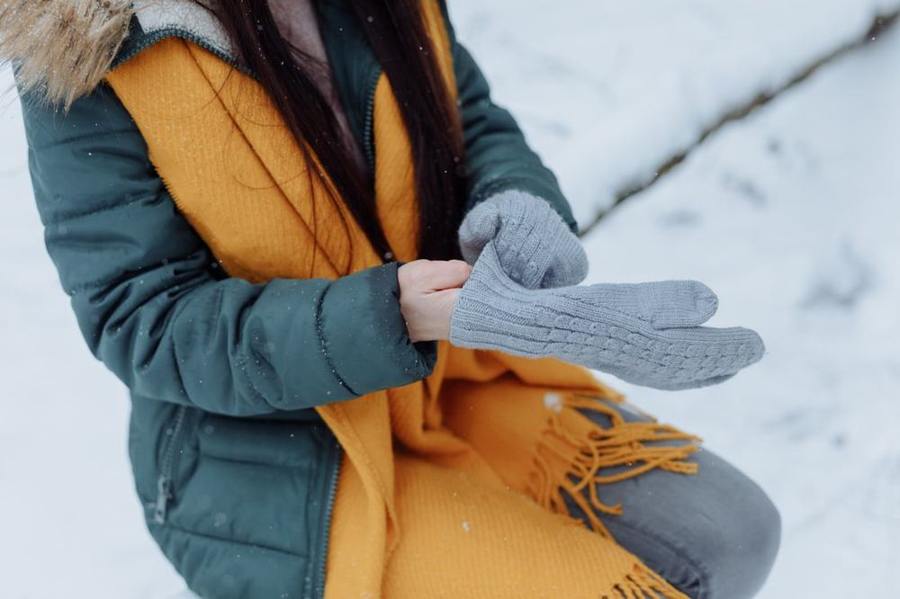 A person puts on a grey glove outdoors in the snow.