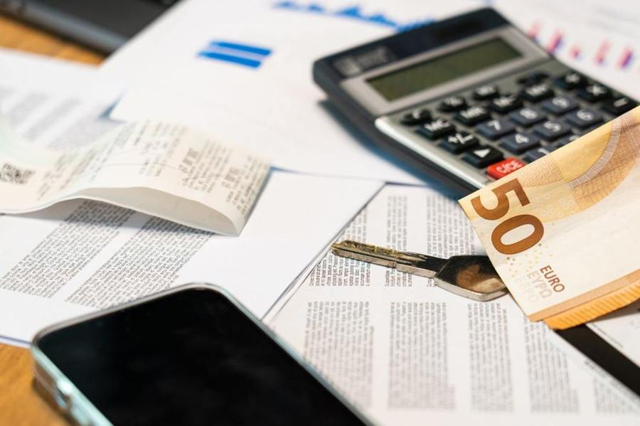 A calculator, euro banknotes and a smartphone lie on paperwork.
