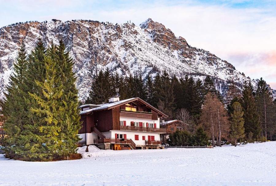 A chalet stands beside a snowy meadow below steep mountains.