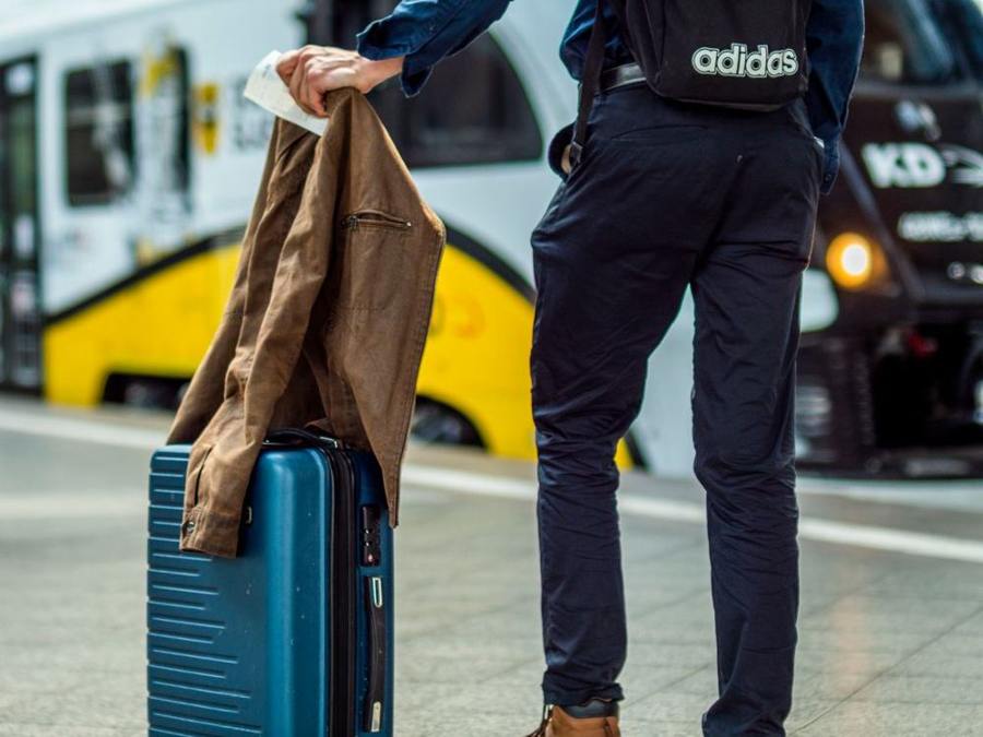 A traveller stands with a rolling suitcase on a railway platform.