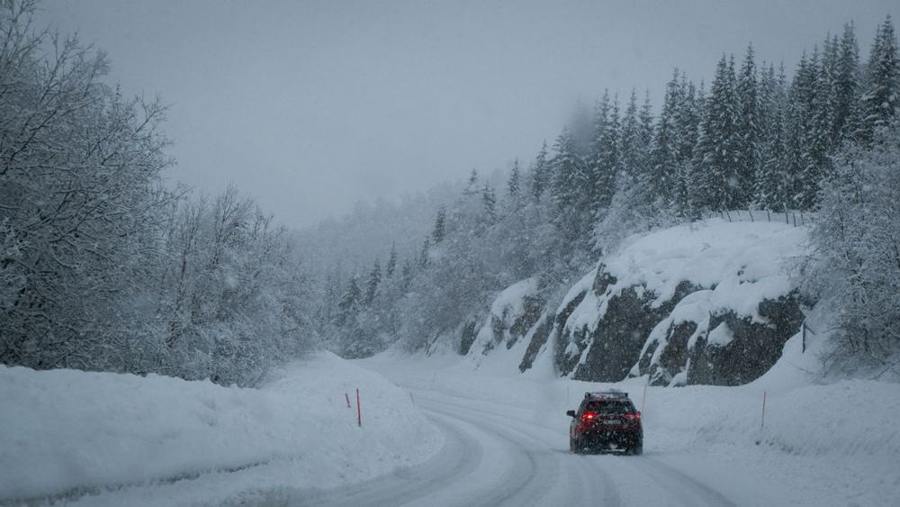 A car travels along a snowy road through a mountain forest.
