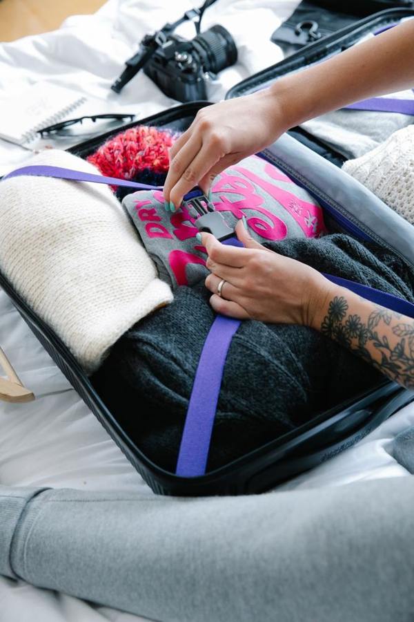 A person packs winter clothing into an open suitcase.