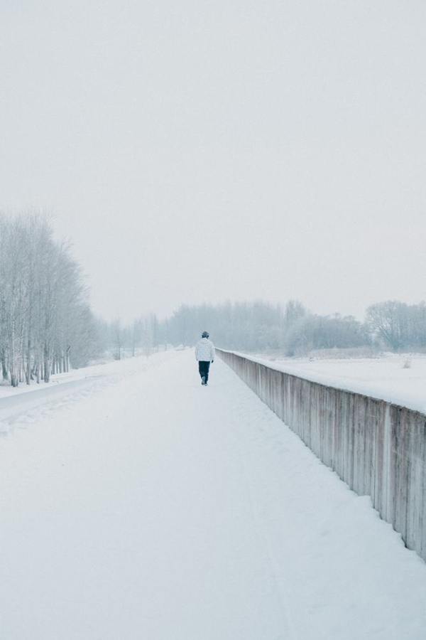 A person walks along a broad snowy path with a railing.