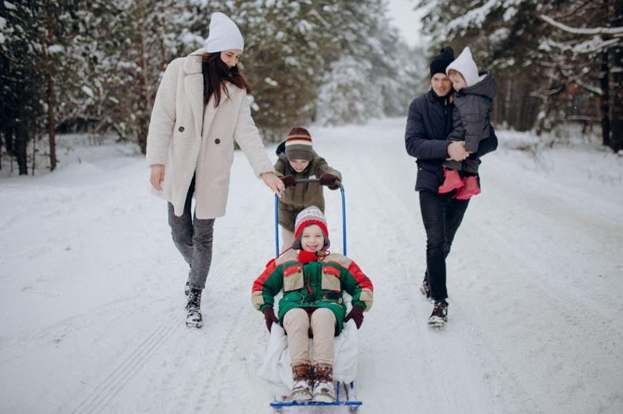 Adults and children travel with a sledge along a snowy forest path.