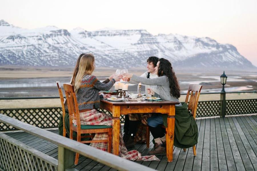 A group sits at a terrace table with snowy mountains beyond.