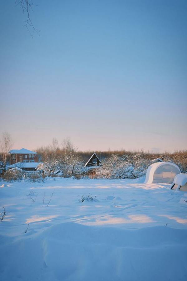 A cabin stands in a snowy landscape in early daylight.