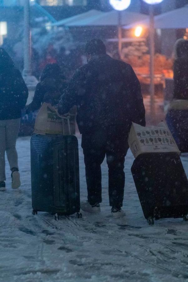 A person pulls two rolling suitcases across snowy ground.