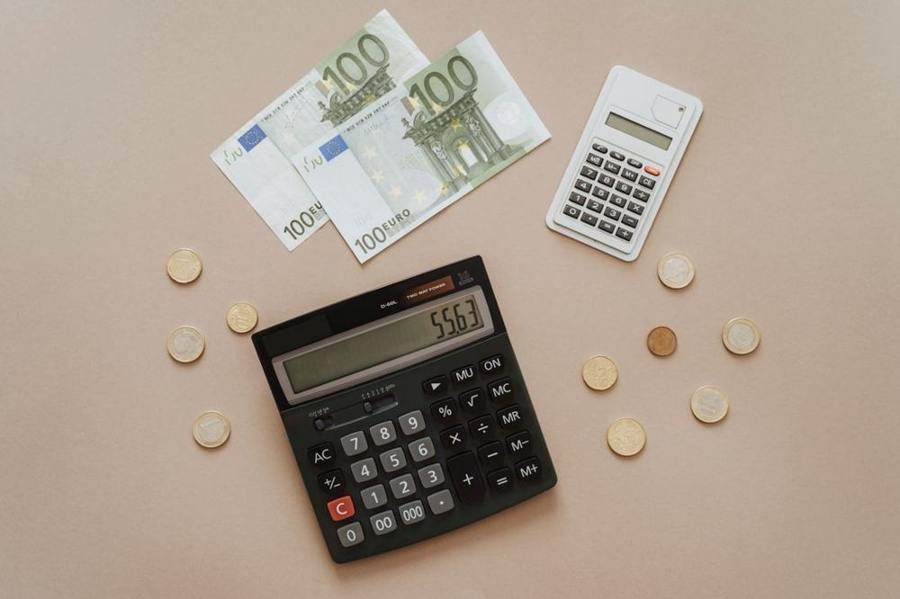 Euro banknotes and coins lie beside two calculators.