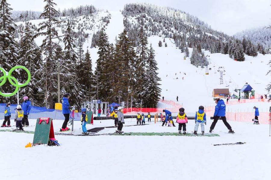 A group of children practises on skis in a marked snowy learning area.