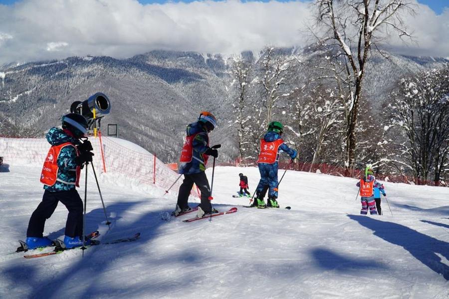 Children wearing helmets practise together on skis on a snowy slope.
