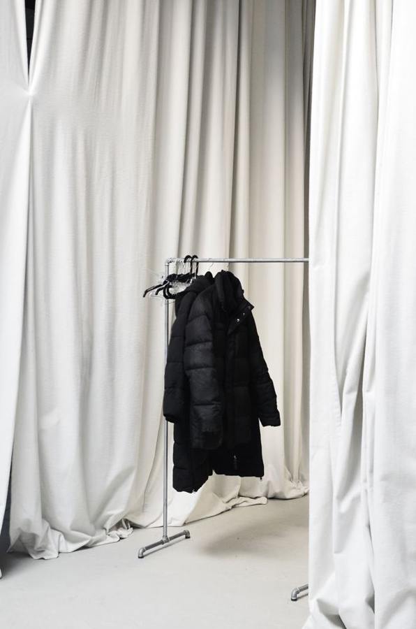 A dark winter jacket hangs on a clothing rack beside curtains.