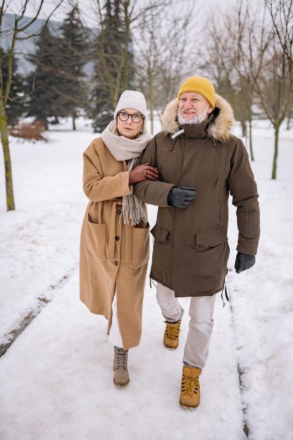 An older couple walks together through a snowy park.