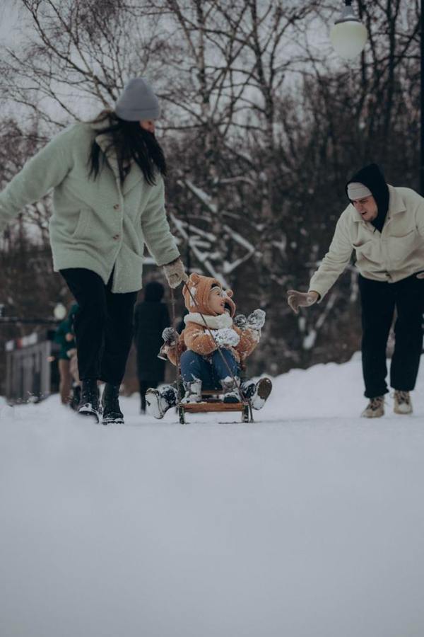 Two adults pull children on a sledge along a forest path.