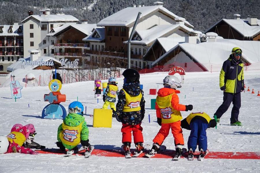 Children in colourful ski clothing stand together in a practice area.