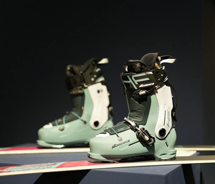 Two pale green alpine ski boots stand on skis in an indoor display.