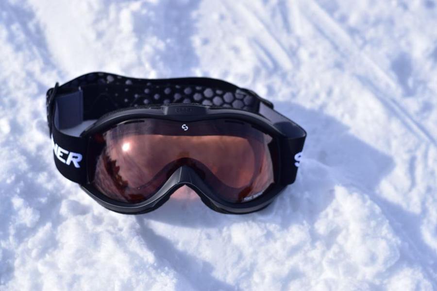 Ski goggles rest on snow with the outer lens facing upwards.