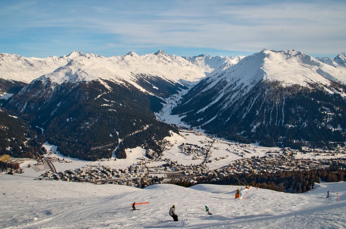 Winter sports participants on a wide slope above Davos with snow-covered mountains beyond.